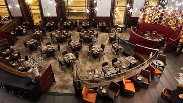 Um restaurante amplo com várias áreas de refeições, incluindo cabines e mesas, e uma área central com parede de destaque vermelha.