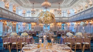 Ein prächtiger Ballsaal mit aufwendigen Kronleuchtern, eleganten floralen Tischdekorationen und komfortablen Sitzgelegenheiten.