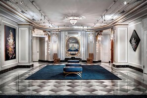 A grand hallway with a checkered floor, a central blue rug, and ornate wall decorations.