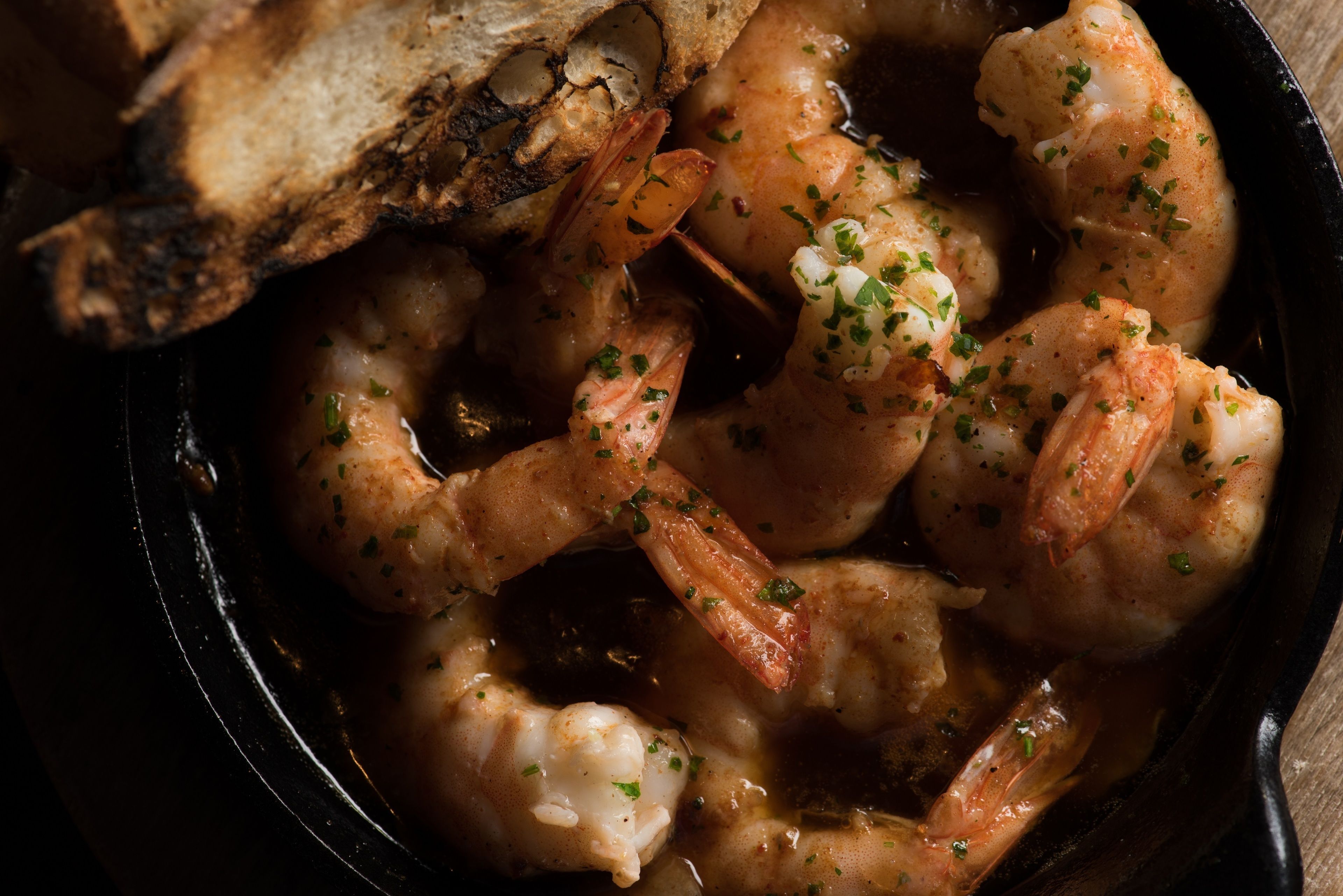 A close-up of a dish with shrimp and bread in a cast iron skillet.