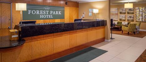 Een receptiebalie bij het Forest Park Hotel, met een houten paneelontwerp, een digitaal scherm en een zithoek met een bank en stoelen op de achtergrond.