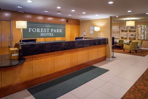 A reception desk at the Forest Park Hotel with a wooden panel design, a digital display, and a seating area with a couch and chairs in the background.