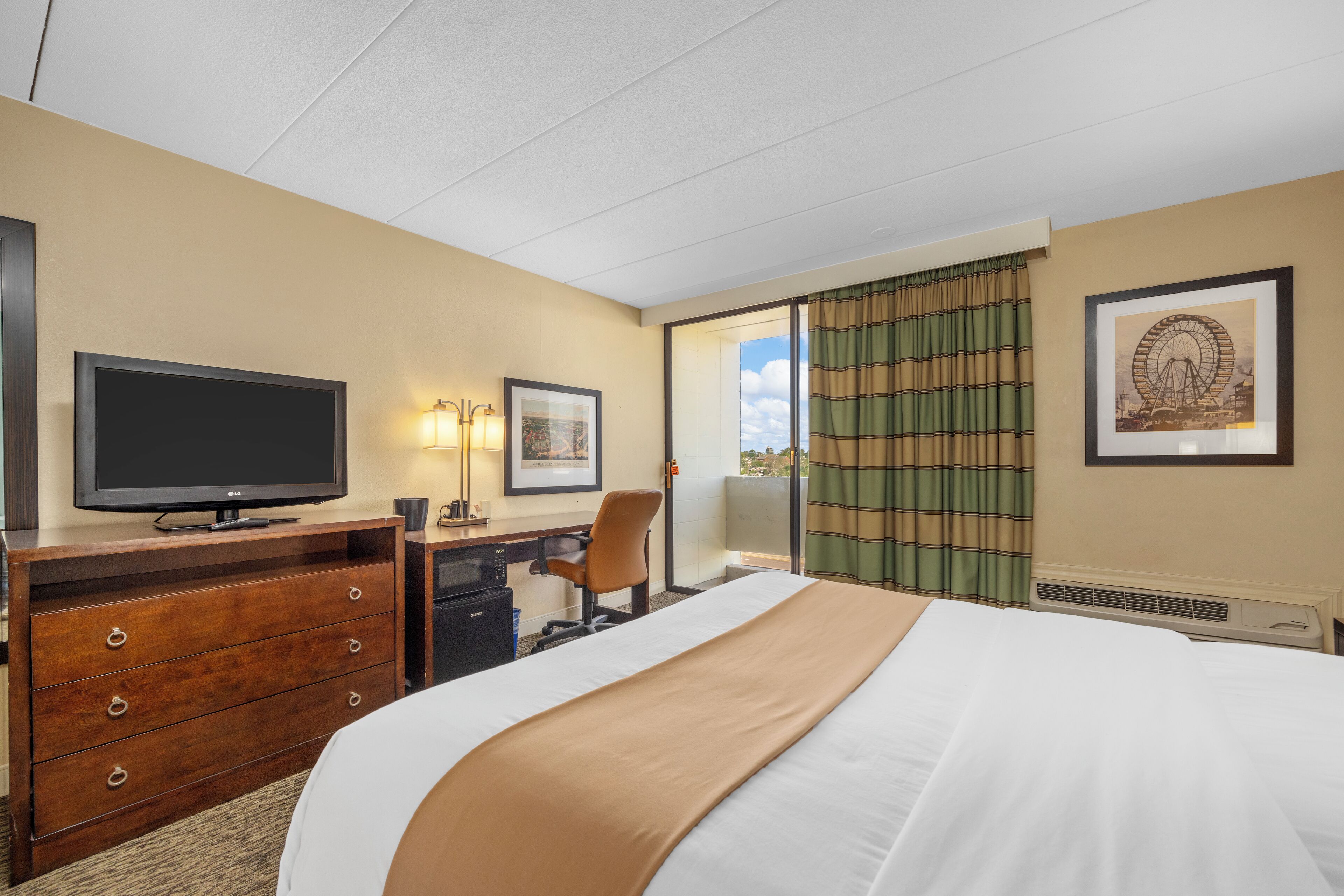 Una habitación de hotel con cama, escritorio, televisor, cómoda y ventana con cortinas.