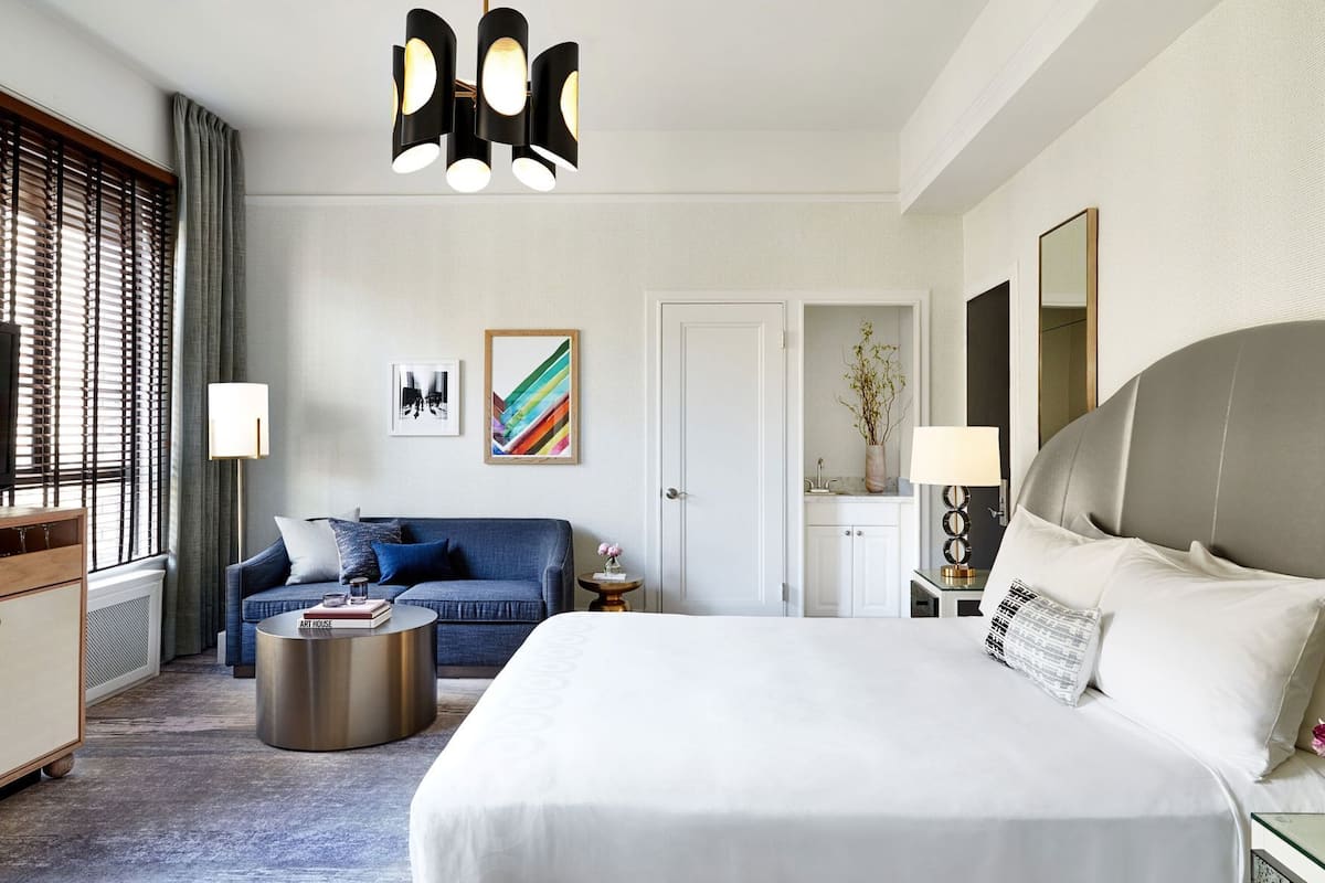 Habitación de hotel con una cama grande, un sofá, una mesa de centro redonda y un escritorio con lámpara.