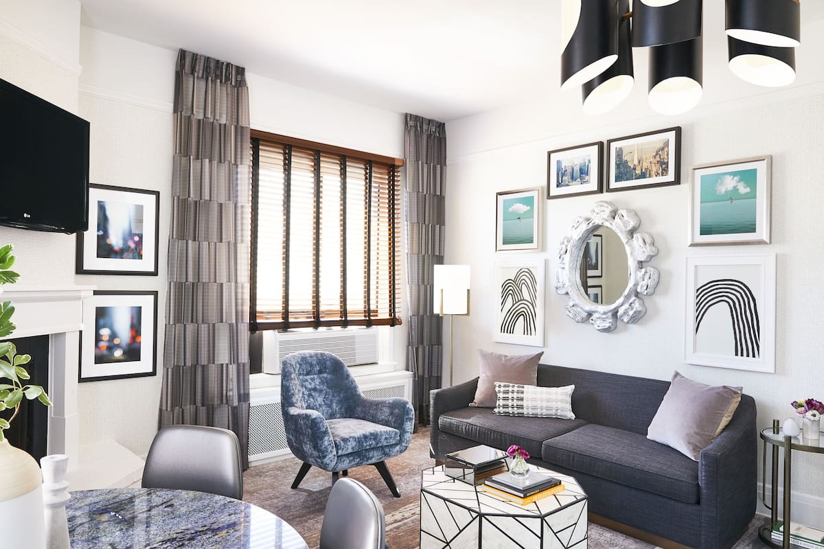 Una sala de estar moderna con un sofá gris, un sillón azul, una mesa de centro y un televisor montado en la pared.