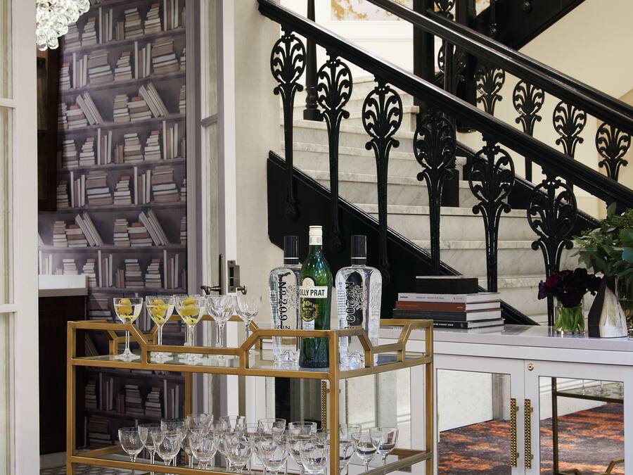 Una scala con ringhiere nere decorate, una libreria con libri e un'area bar con bicchieri e bottiglie.