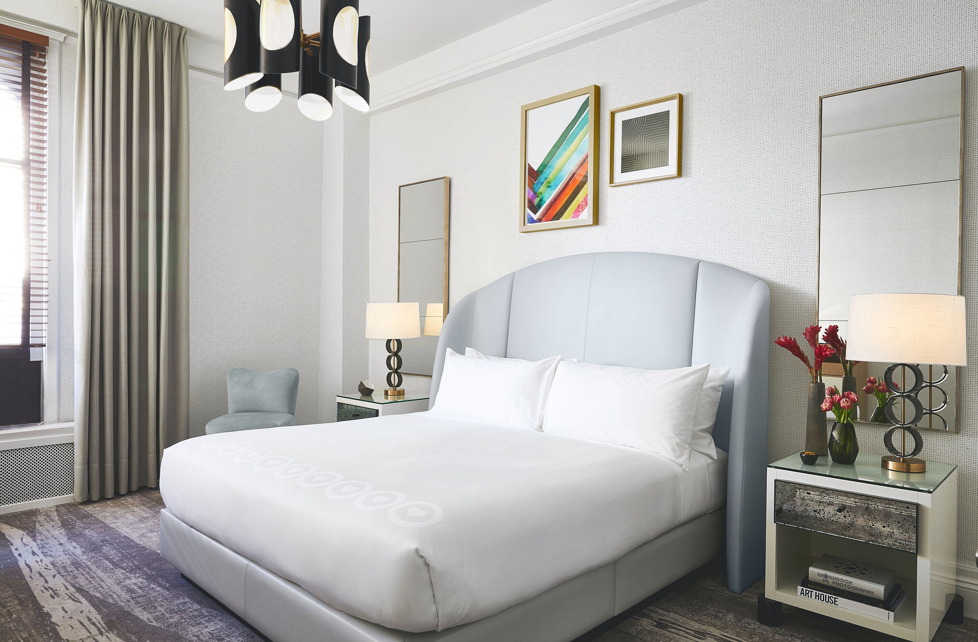 A hotel room with a large bed, a nightstand with a lamp, a mirror, and artwork on the wall.
