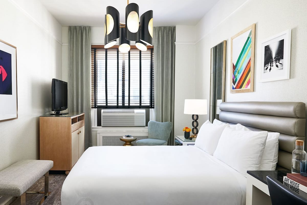 Habitación de hotel con cama, escritorio, silla, televisión, lámpara y obras de arte en las paredes.