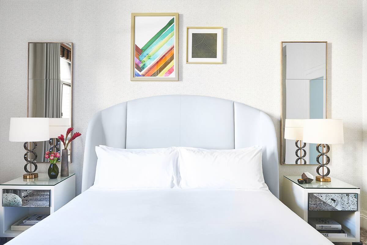 Habitación de hotel con una cama grande, dos mesitas de noche con lámparas y dos cuadros en la pared.