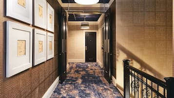 Un pasillo con cuadros enmarcados en las paredes, alfombra estampada y una puerta al final.