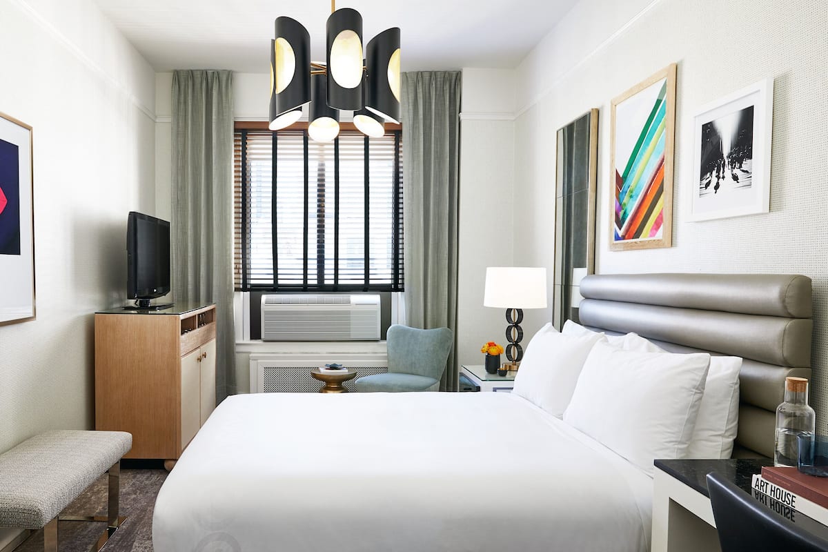 Una habitación de hotel con cama, escritorio, silla, televisor y obras de arte en las paredes.