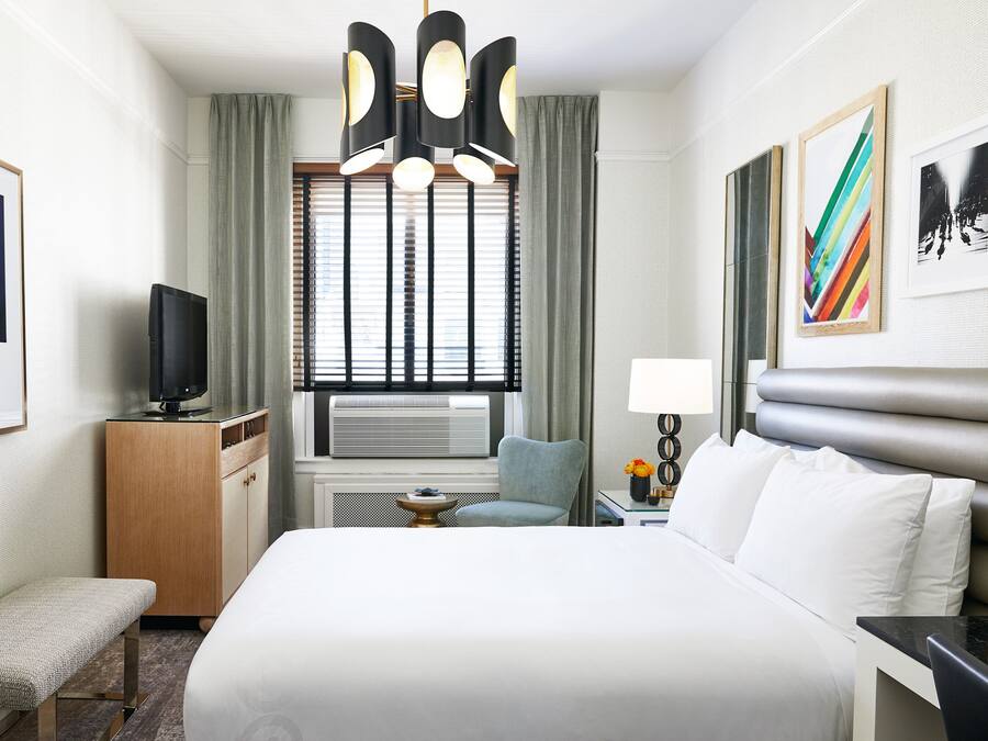 Quarto de hotel com cama, escrivaninha, cadeira, televisão e obras de arte nas paredes.