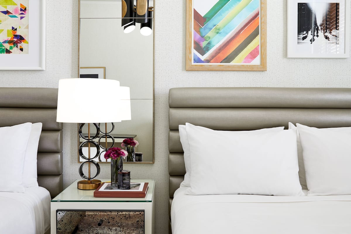 Habitación de hotel con diseño moderno, que incluye una cama grande, una mesita de noche con lámpara y obras de arte en las paredes.