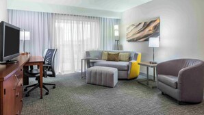 A hotel room with a desk, a sofa, an ottoman, a chair, a TV, a lamp, and a painting on the wall. - Courtyard by Marriott Knoxville Cedar Bluff (Knoxville)