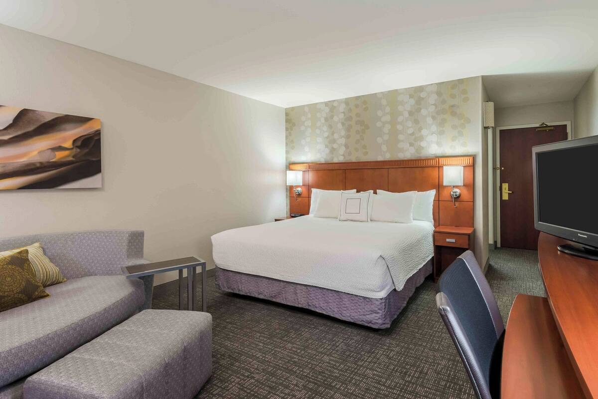 Una habitación de hotel con una cama, un sofá, un televisor y un cuadro en la pared.