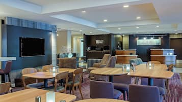 Un moderno vestíbulo de hotel con varias zonas de estar, un televisor de pantalla plana y una recepción.
