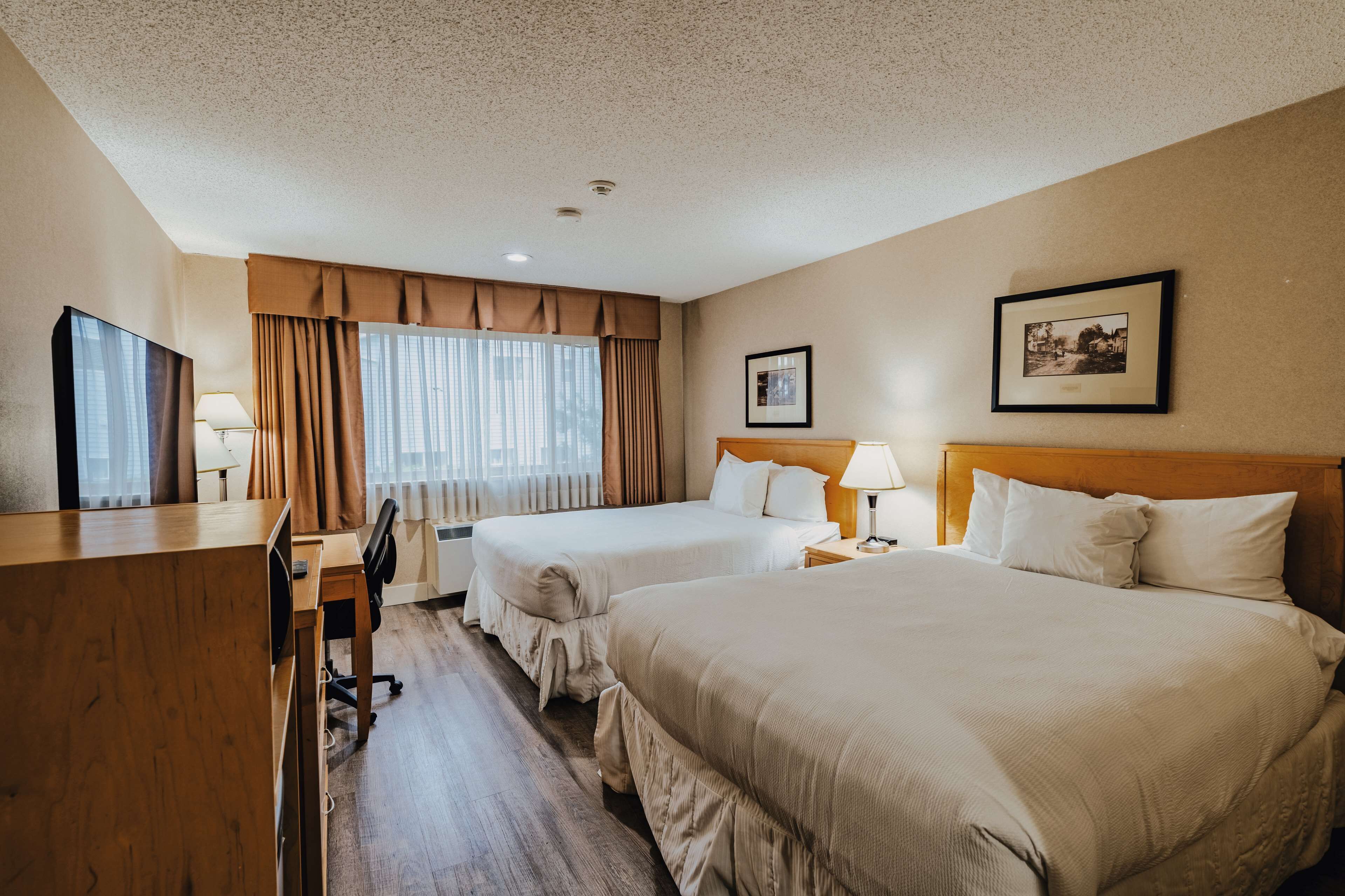 A hotel room with two beds, a desk, a chair, a TV, and a window with curtains.