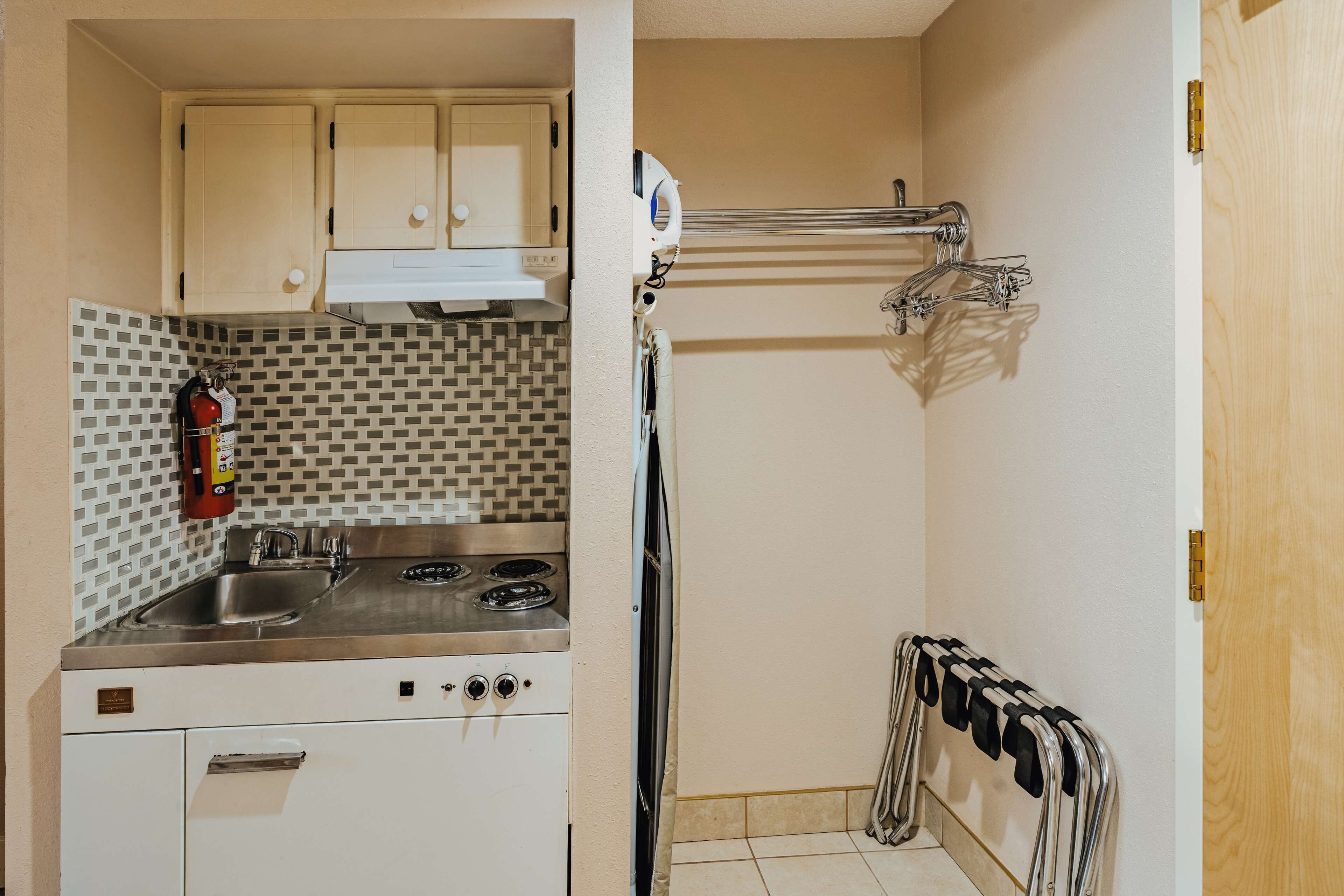 Cocina compacta con estufa a gas, pileta y gabinetes blancos. Se observa un extintor de incendios en la pared y un perchero con varias toallas.