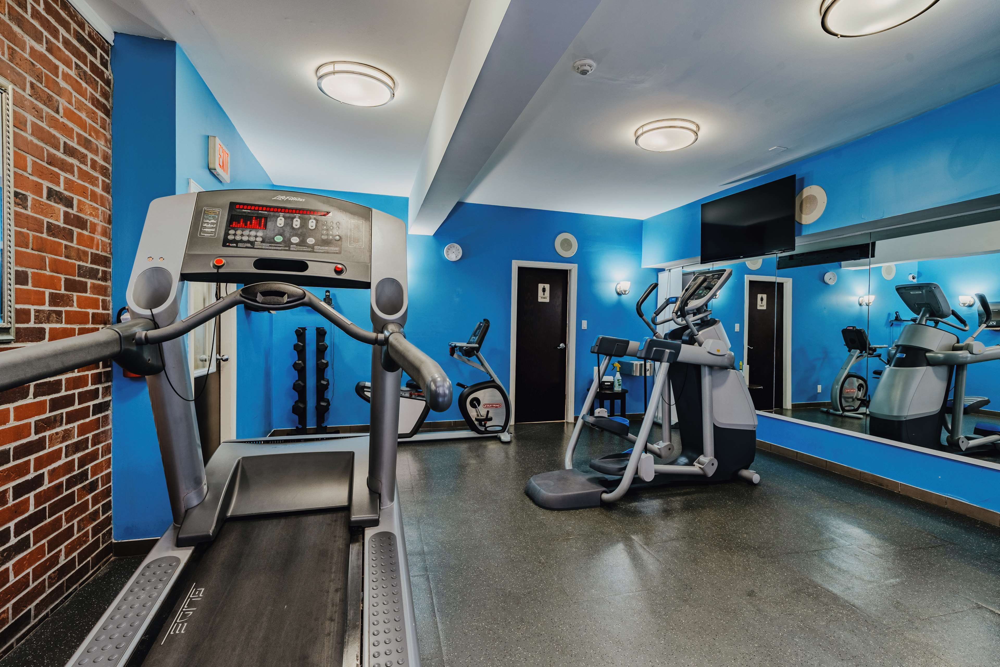 A gym with treadmills, elliptical machines, and a mirrored wall.