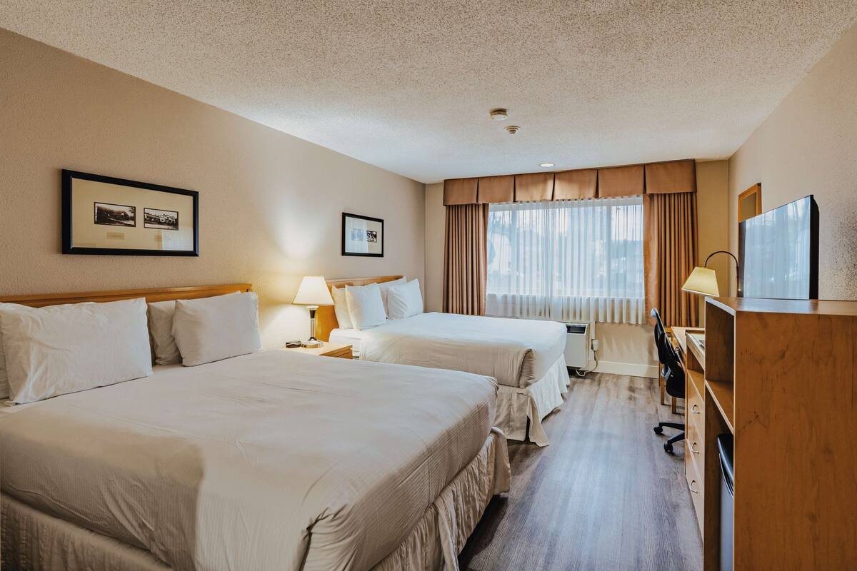 Habitación de hotel con dos camas, un escritorio, una silla y un televisor.