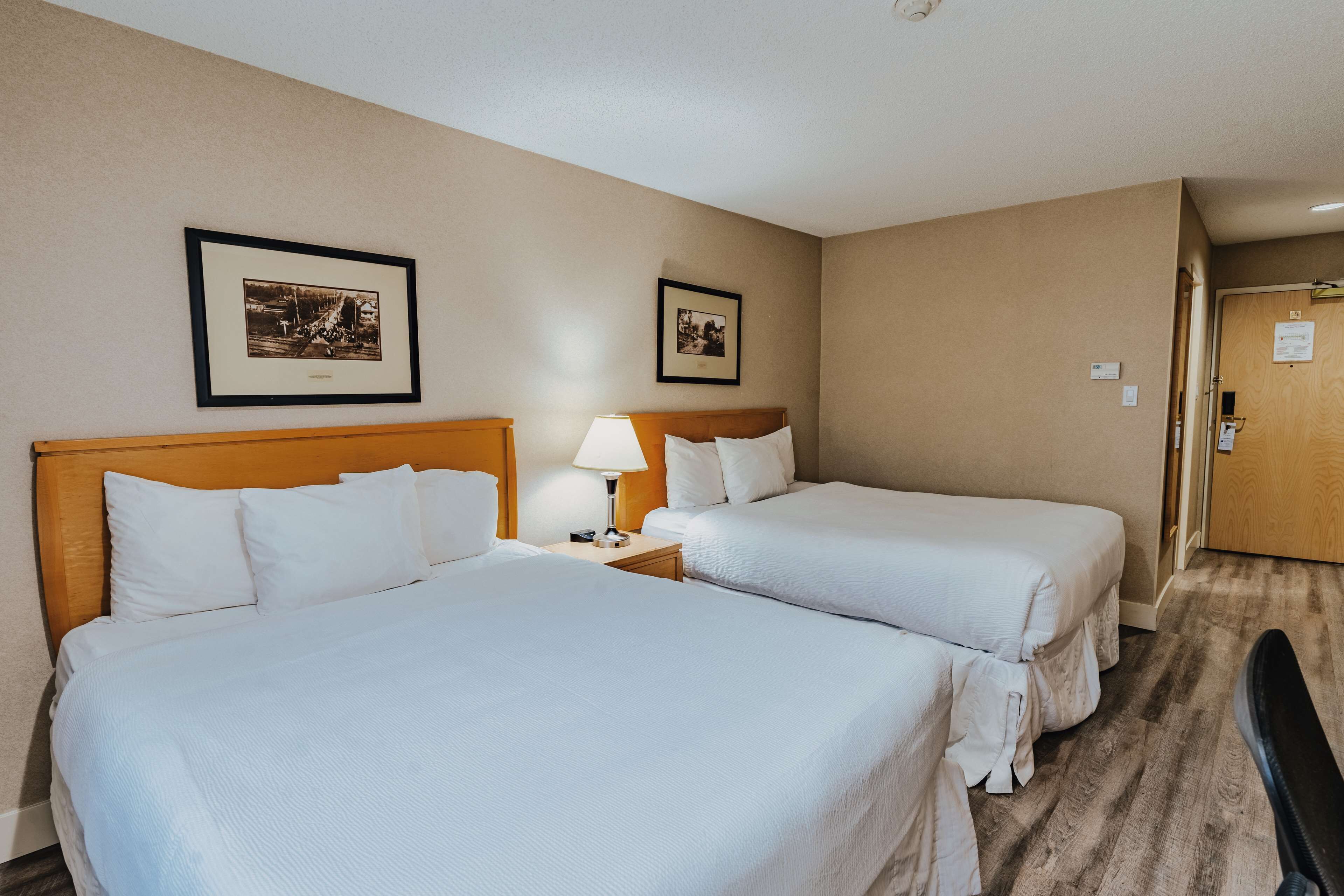 Una habitación de hotel con dos camas, una mesita de noche con lámpara y cuadros en la pared.