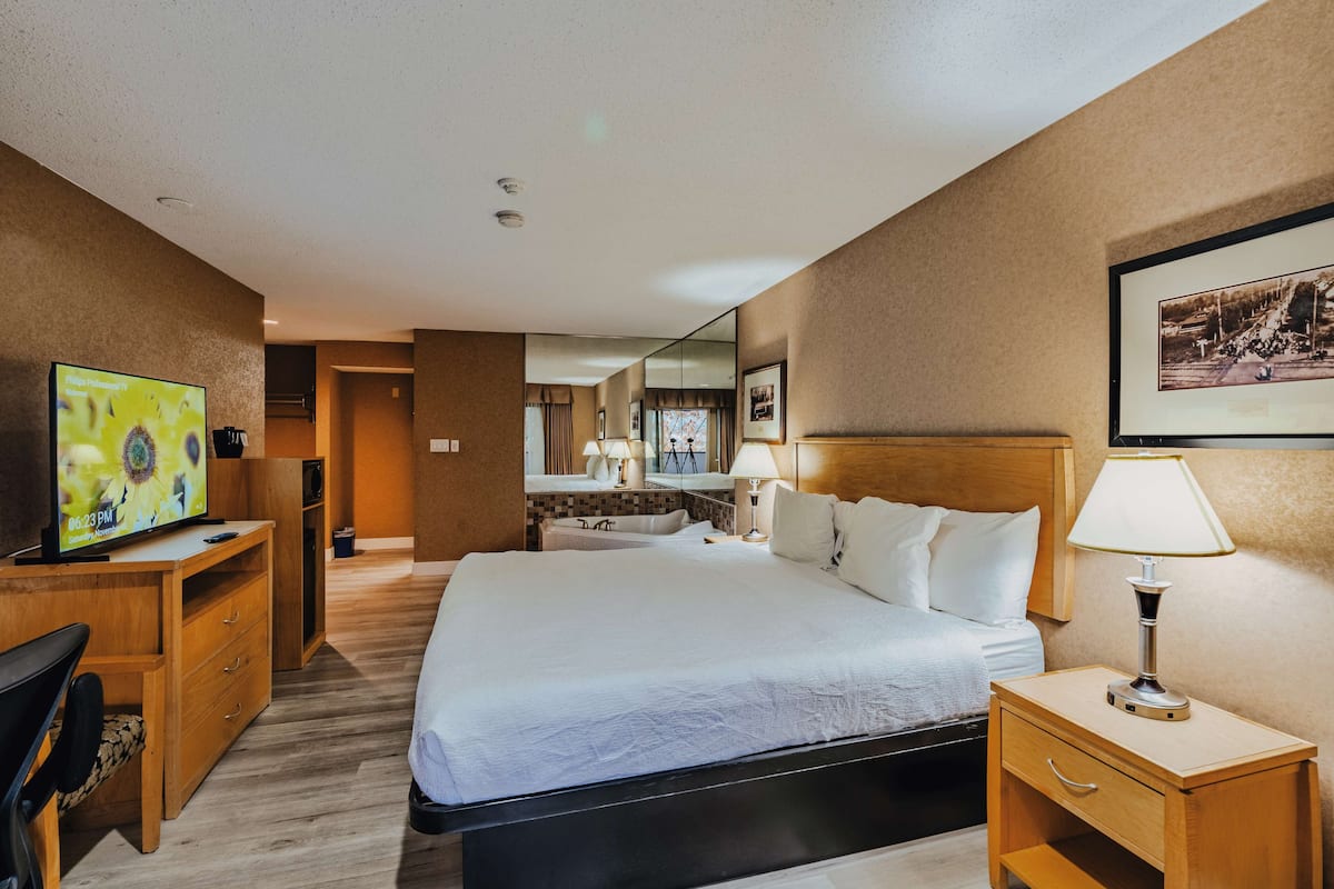 Habitación de hotel con una cama grande, mesita de noche con lámpara, escritorio con televisor y espejo en la pared.