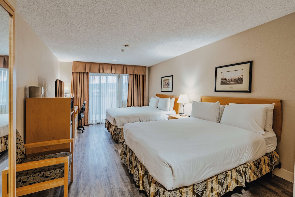 Habitación de hotel con dos camas, un escritorio, una silla y una ventana con cortinas.
