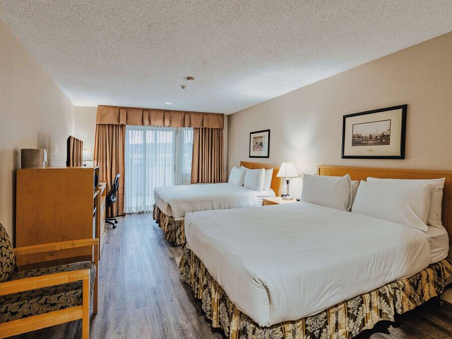 Ein Hotelzimmer mit zwei Betten, einem Schreibtisch, einem Stuhl und einem fenster mit Vorhängen.