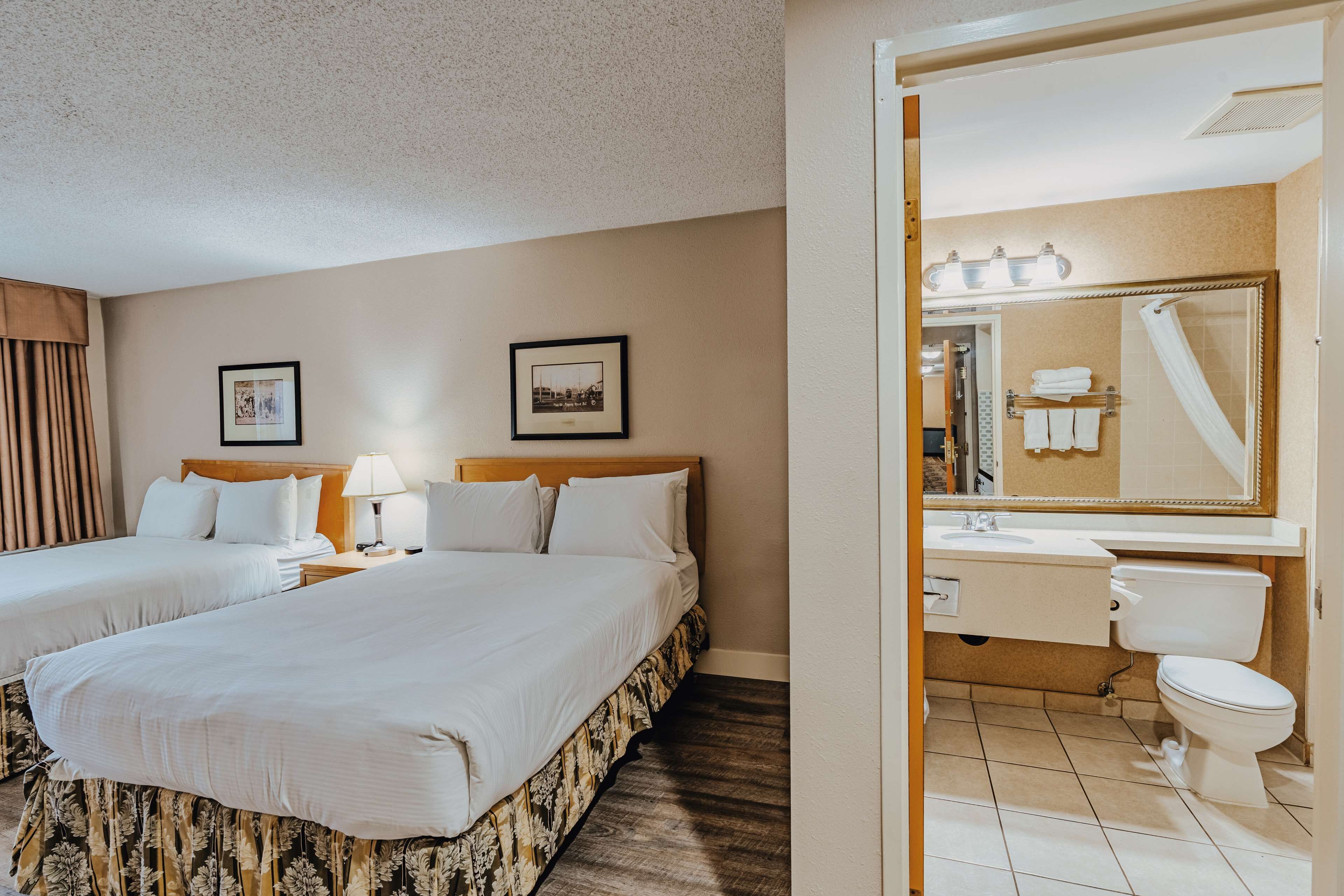 A hotel room with two beds, a bathroom with a shower, and a vanity with a mirror.