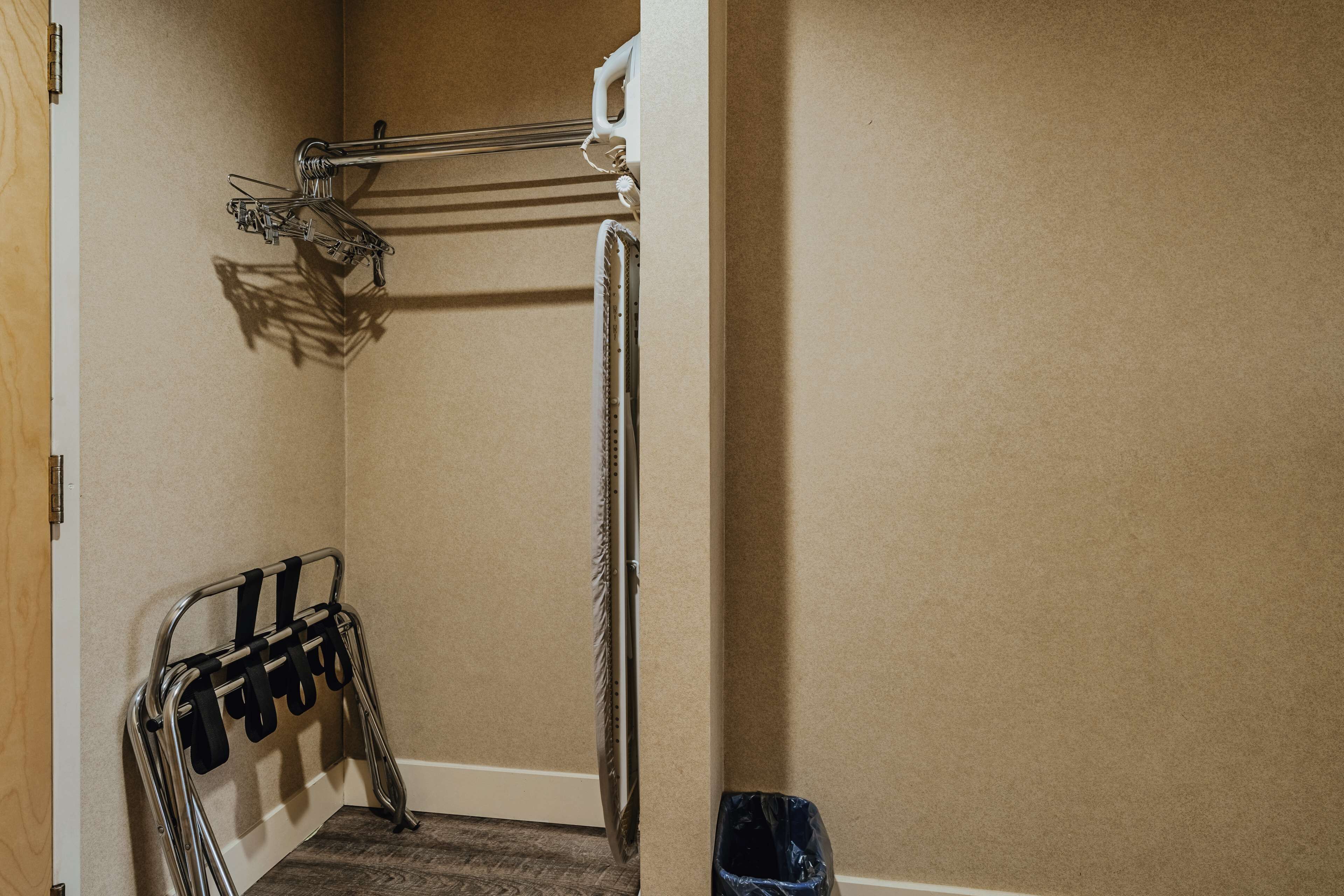 A corner of a room with a metal rack holding black items, a white door frame, and a black trash bin.