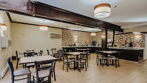 A restaurant with multiple tables and chairs, a kitchen area, and a counter with a menu.