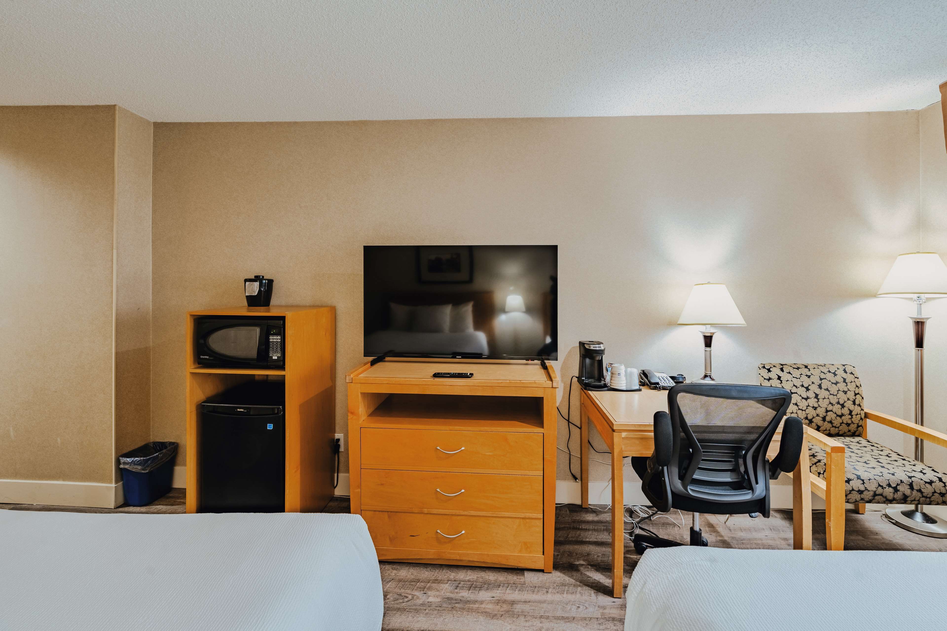 A hotel room with a bed, a desk with a computer, a chair, a television, and a microwave.