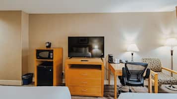 A hotel room with a bed, a desk with a computer, a chair, a television, and a microwave.