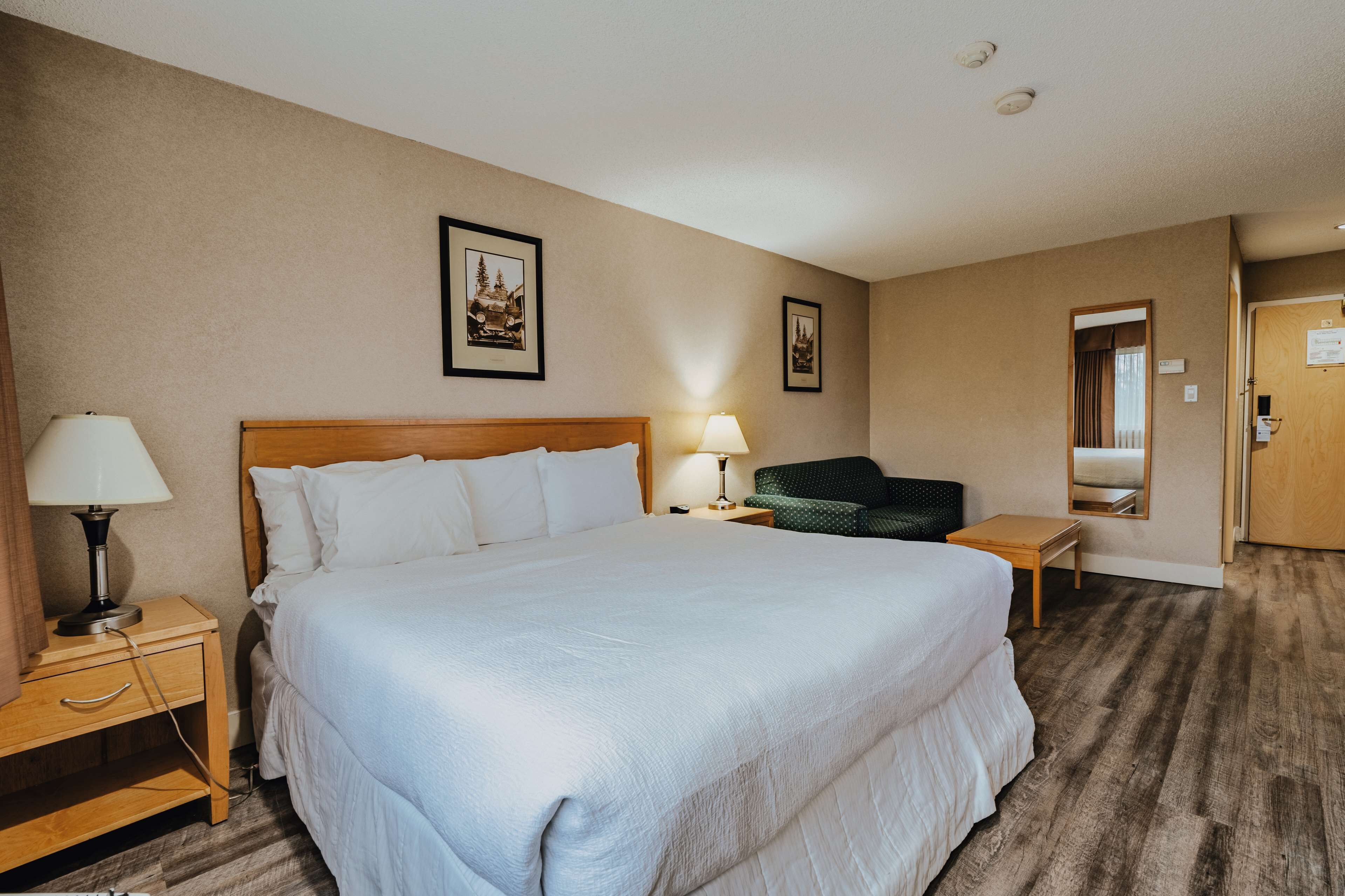 Una habitación de hotel con una cama grande, dos mesitas de noche, una silla y un espejo.