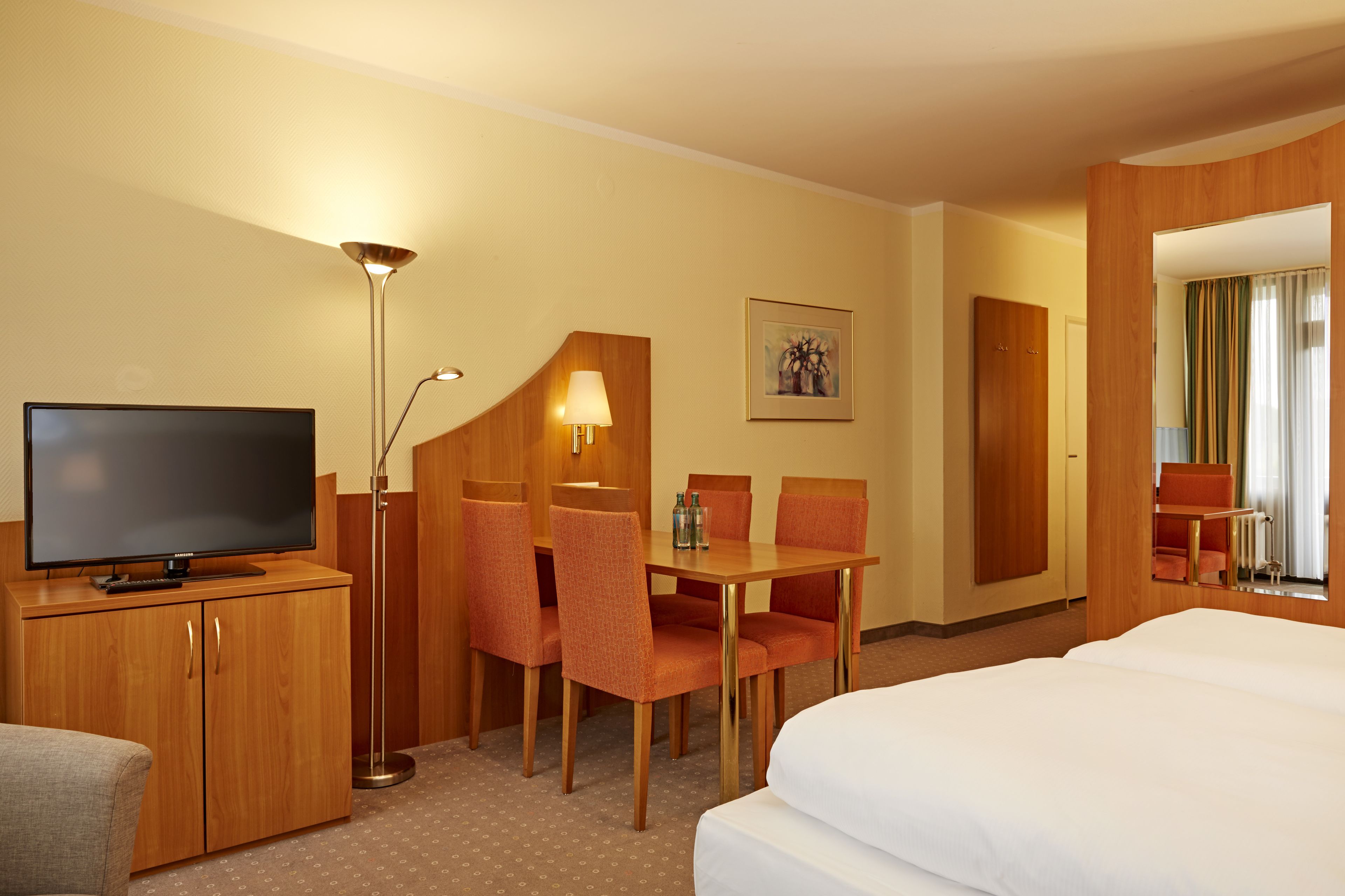 A hotel room with a TV, a desk with chairs, a bed, and a lamp.