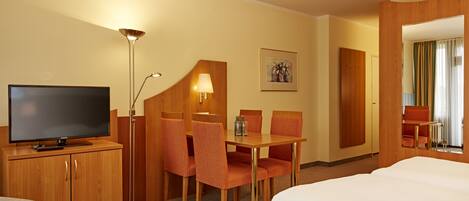 Habitación de hotel con televisión, escritorio con sillas, cama y lámpara.