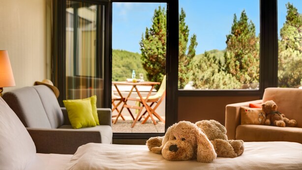 Une pièce confortable avec un lit, un canapé et une fenêtre donnant sur du mobilier d’extérieur et des arbres.