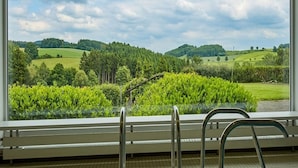 A room with a large window offering a view of a green landscape with trees and hills. - Sunday Hotel Willingen (Willingen)