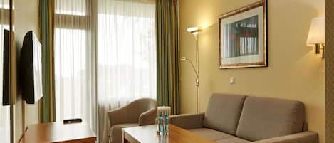 A hotel room with a sofa, a small table, a TV, and a painting on the wall.