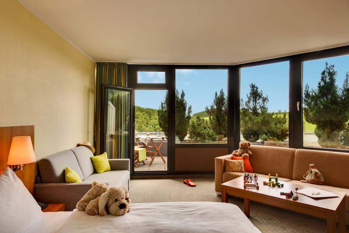 A hotel room with a bed, a sofa, a coffee table, and a view of the outdoors.