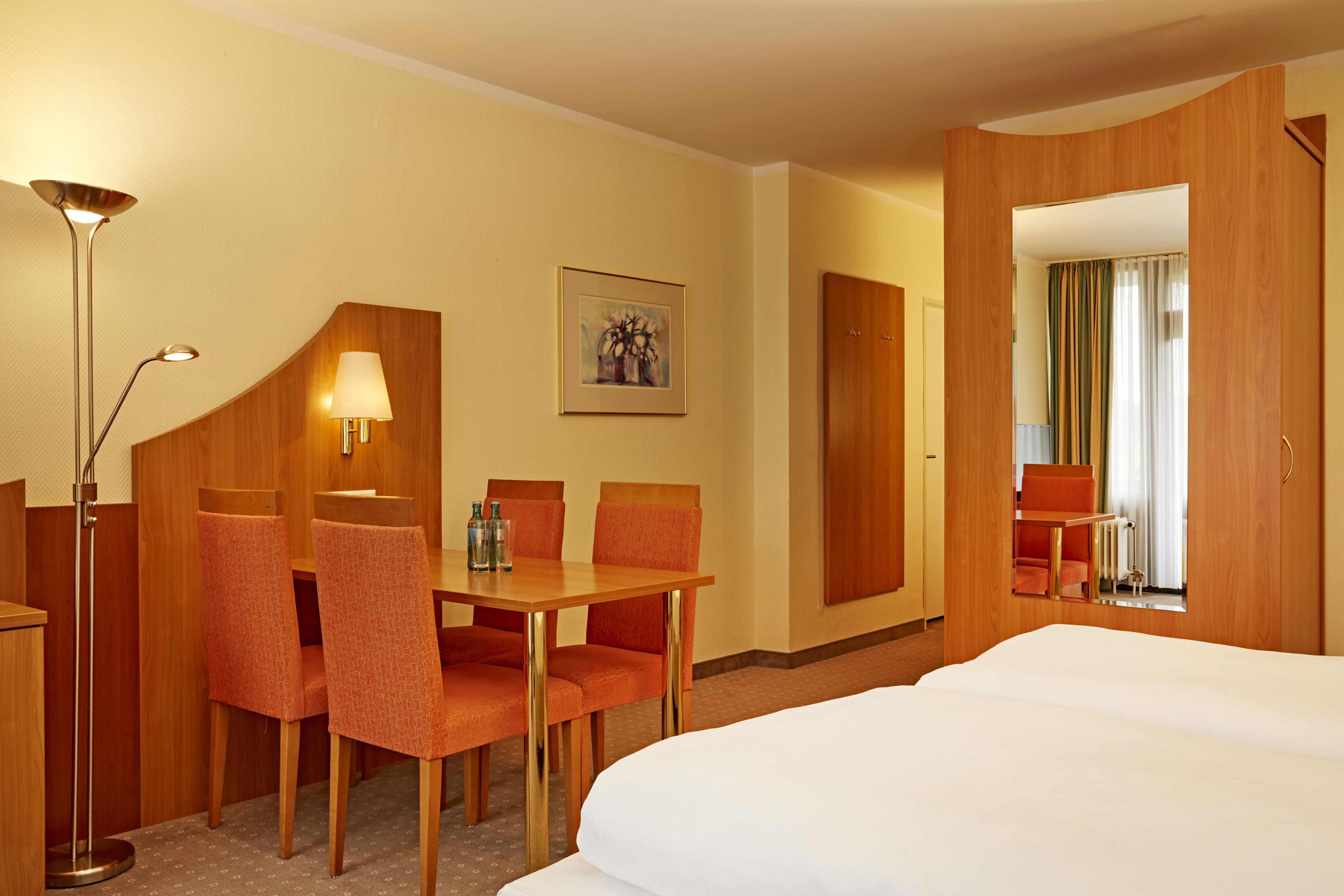 Ett hotellrum med en säng, ett skrivbord med två stolar, en lampa och en inramad tavla på väggen.
