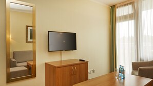 Une chambre d’hôtel avec un bureau en bois, un téléviseur fixé au mur, un miroir et une fenêtre avec des rideaux légers.