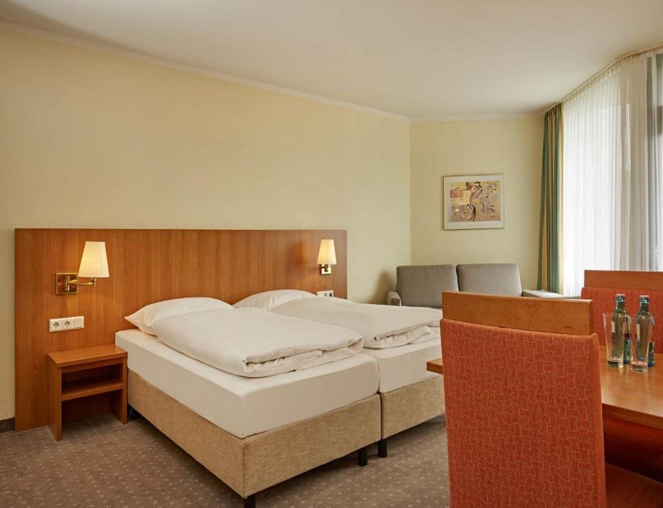 Une chambre d’hôtel avec deux lits, un bureau, une chaise et une petite table sur laquelle se trouvent des bouteilles.