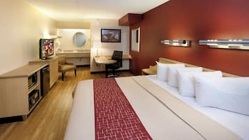Ett hotellrum med en säng, ett skrivbord, en stol, en tv, en spegel och en väggmonterad lampa.