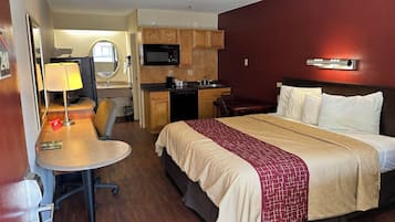 Une chambre d’hôtel équipée d’un lit, d’un bureau, d’une chaise, d’une kitchenette et d’un miroir.