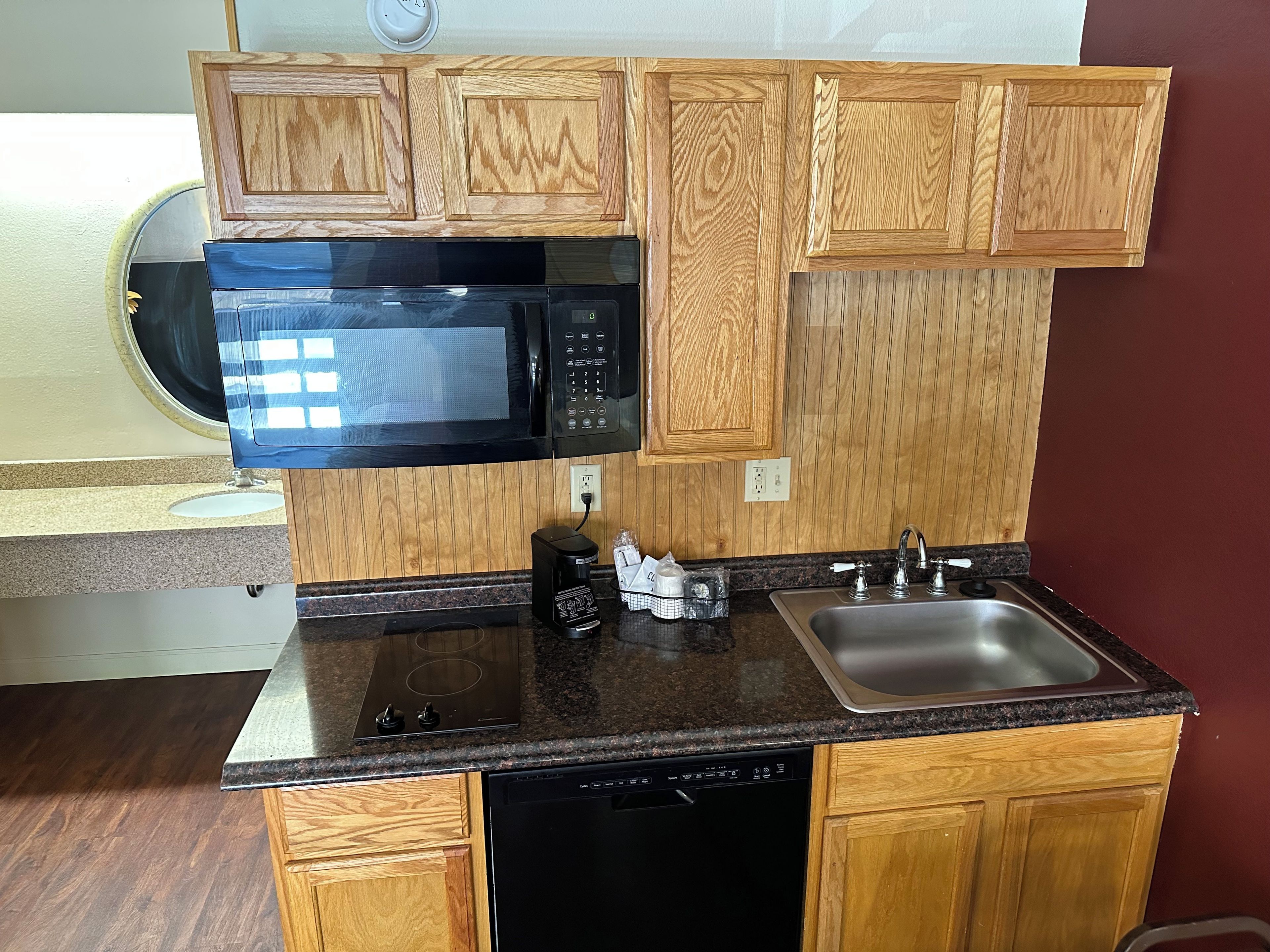 Cocina compacta con armarios de madera, microondas negro, cafetera y un lavamanos.