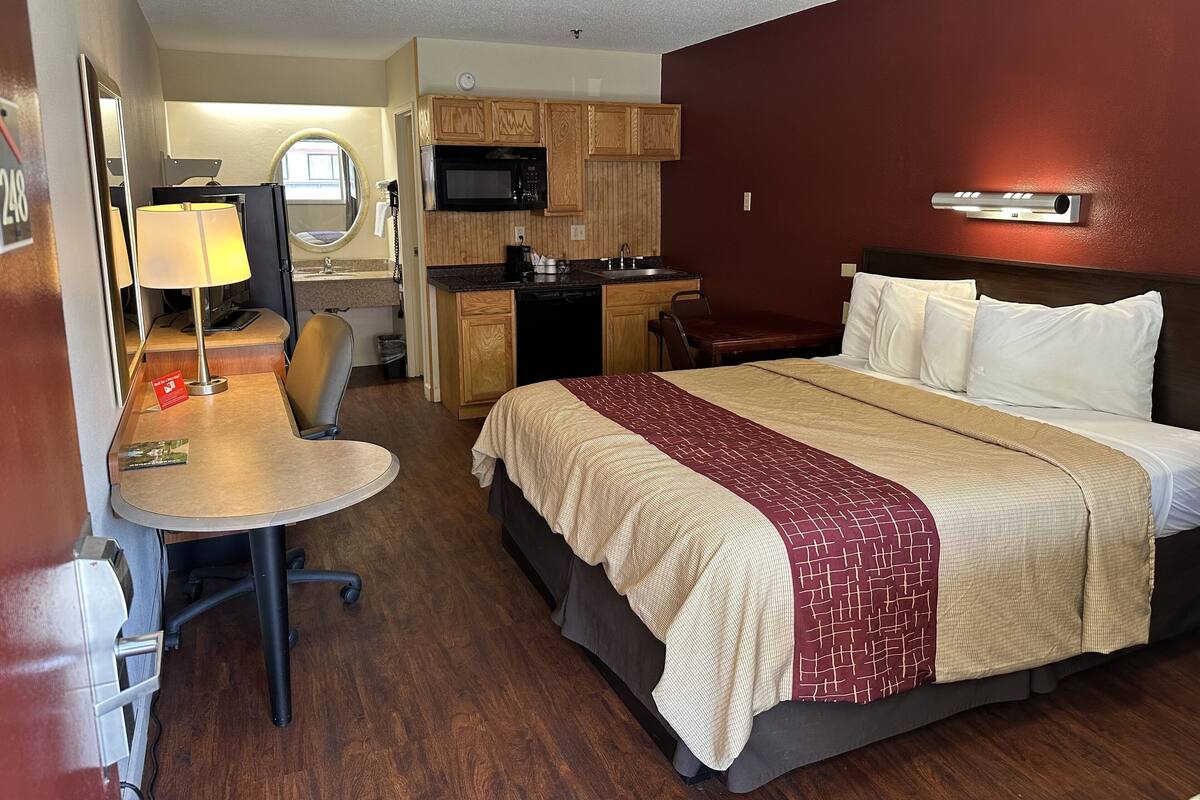 A hotel room with a bed, a desk with a chair, a microwave, and a small kitchenette.