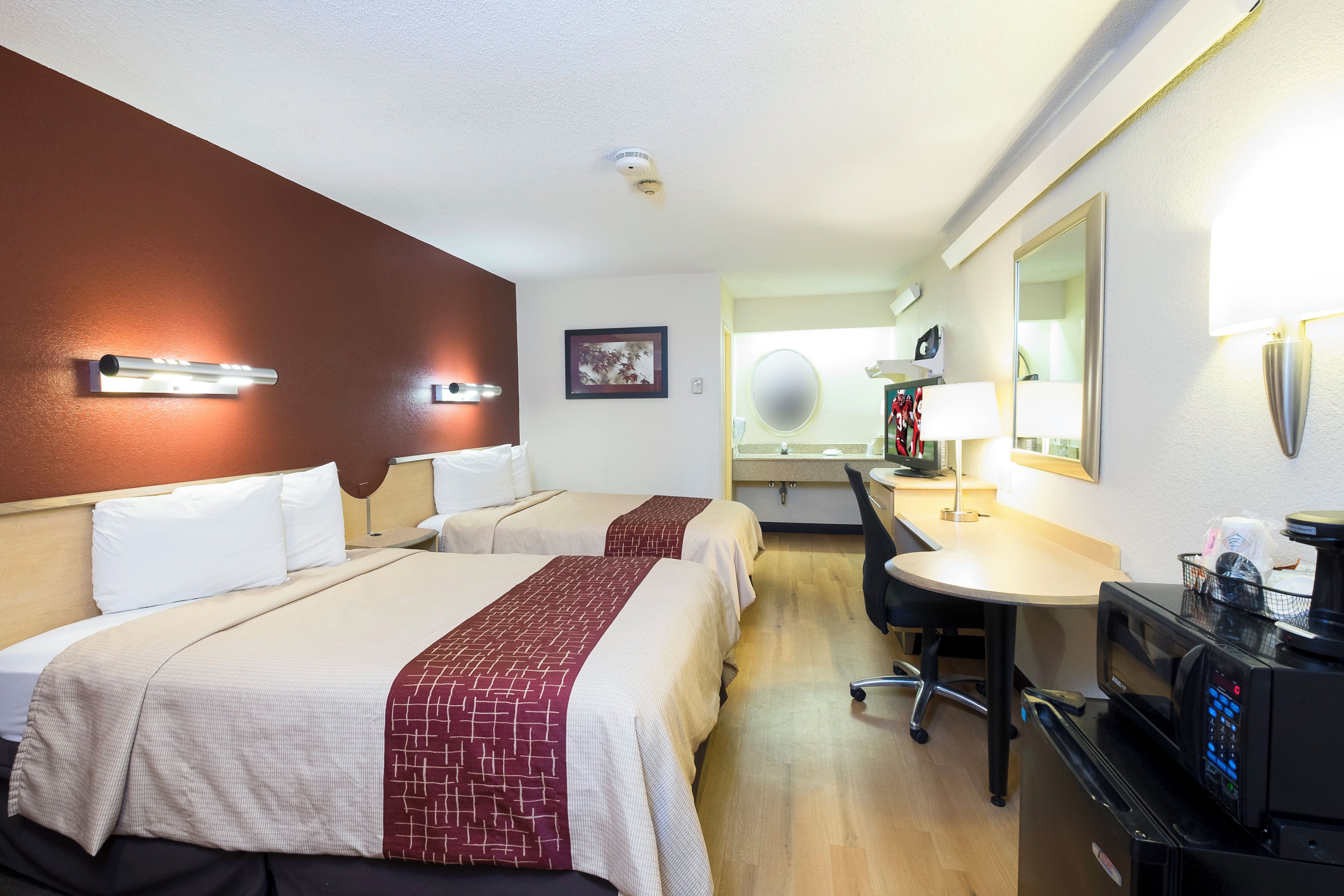 A hotel room with two beds, a desk, a chair, a TV, and a minibar.