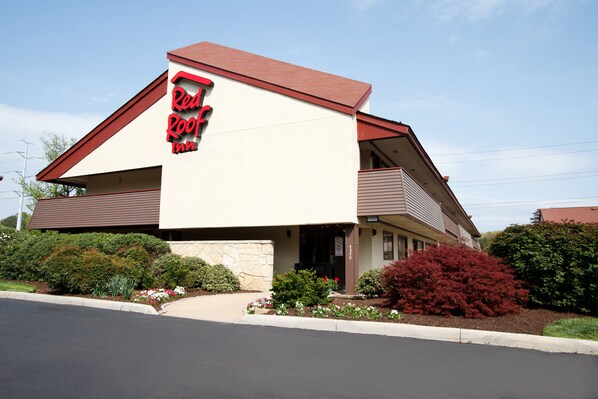 A Red Roof Inn with a modern design, featuring a prominent red and white sign, a sloped roof, and a landscaped front yard with various shrubs and flowers. - Red Roof Inn Parkersburg (Parkersburg)