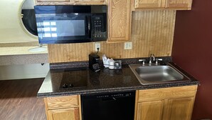A compact kitchen with wooden cabinets, a black microwave, a coffee maker, and a sink.